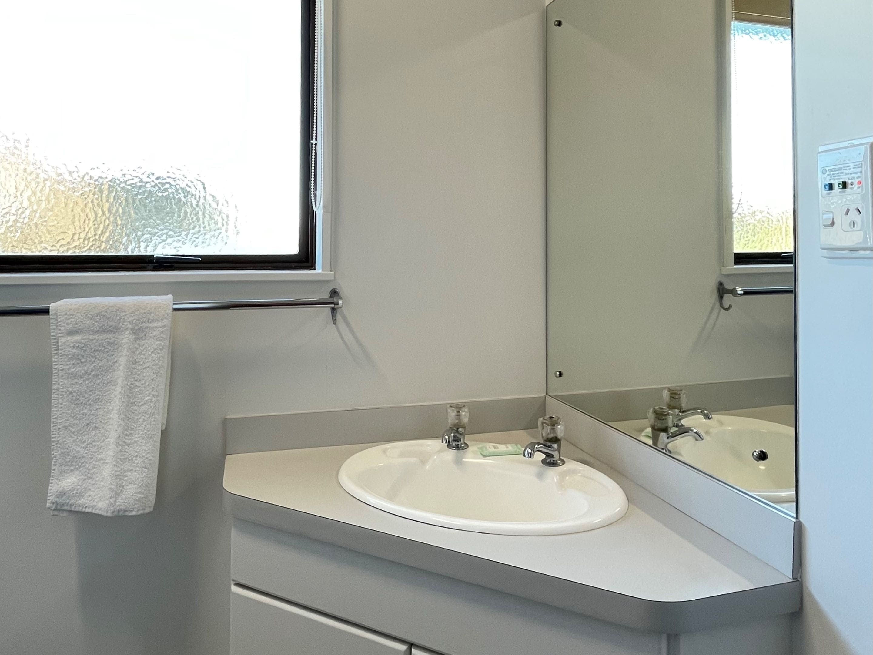 Un baño con un lavamanos blanco, un espejo y una toalla colgada en un perchero.