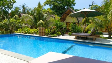 Piscina azul clara con sillas de descanso y una sombrilla, rodeada de exuberante vegetación tropical.