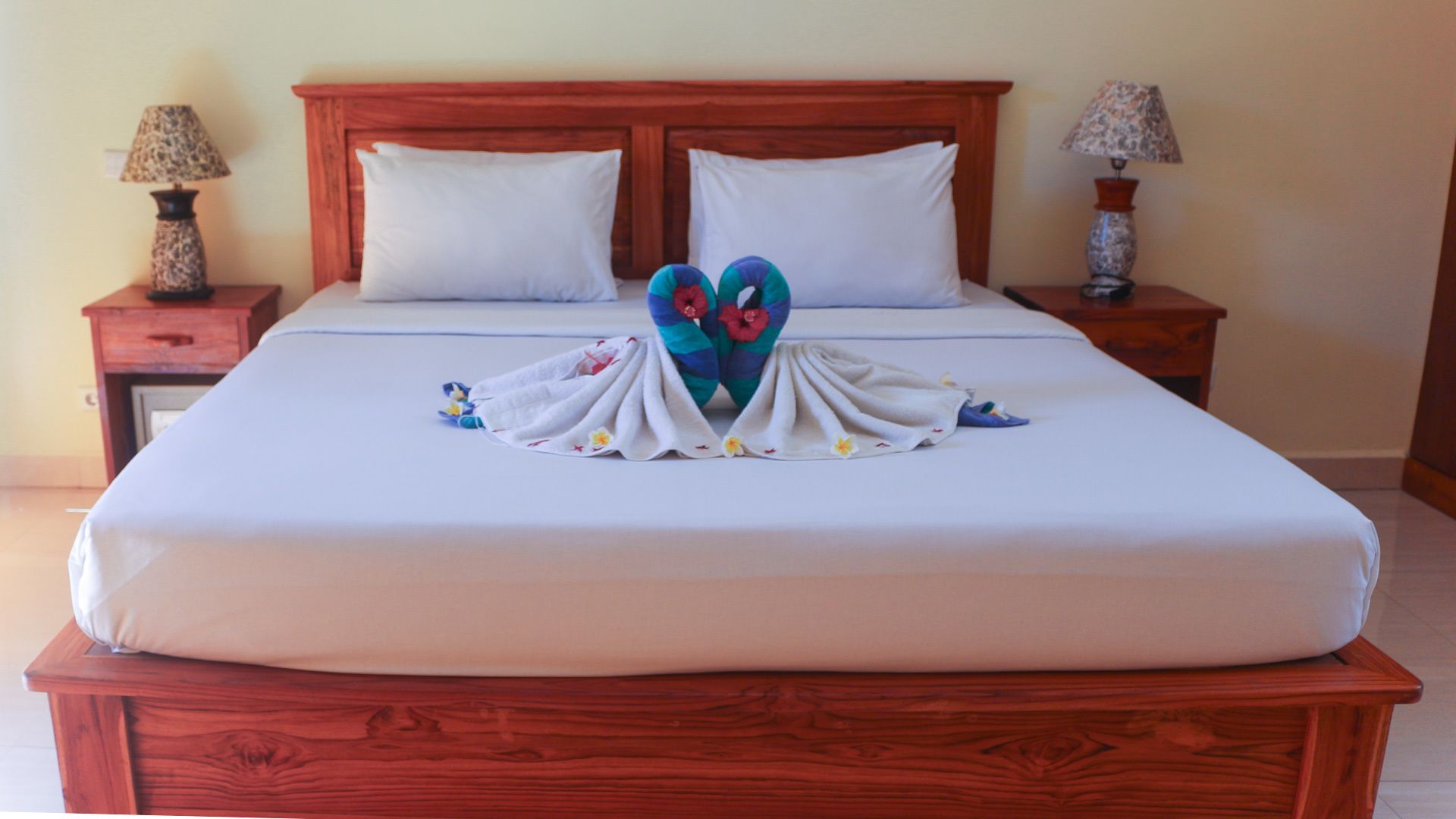 A neatly made bed with a heart-shaped towel arrangement in the center, two white pillows, and a wooden headboard.
