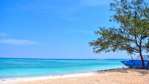 Una playa con agua turquesa cristalina, una orilla de arena y un barco azul.