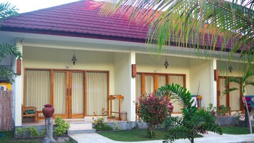 A two-story house with a red tiled roof, wooden doors, and a small porch area with a chair and a table.