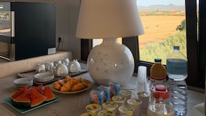 A breakfast table with plates of food, a lamp, and a view of a field through the window. - Il Tramonto (Giba)