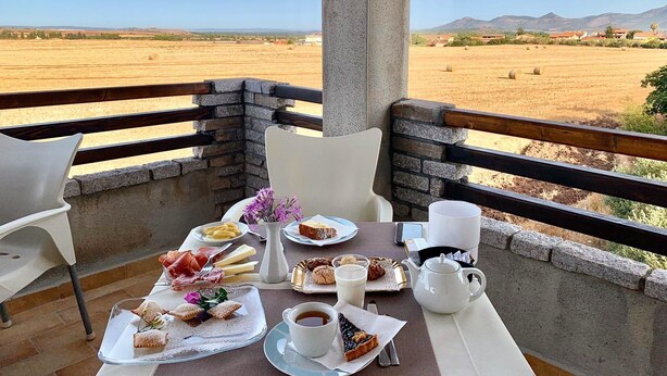 A dining table with food and drinks, overlooking a scenic landscape. - Il Tramonto (Giba)