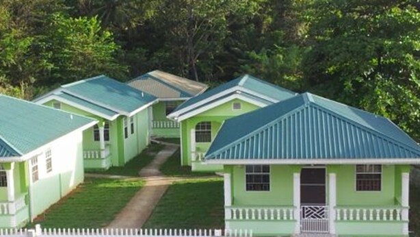 A row of small, single-story cottages with green roofs and white railings, surrounded by greenery. - Digs Cottages (Portsmouth)