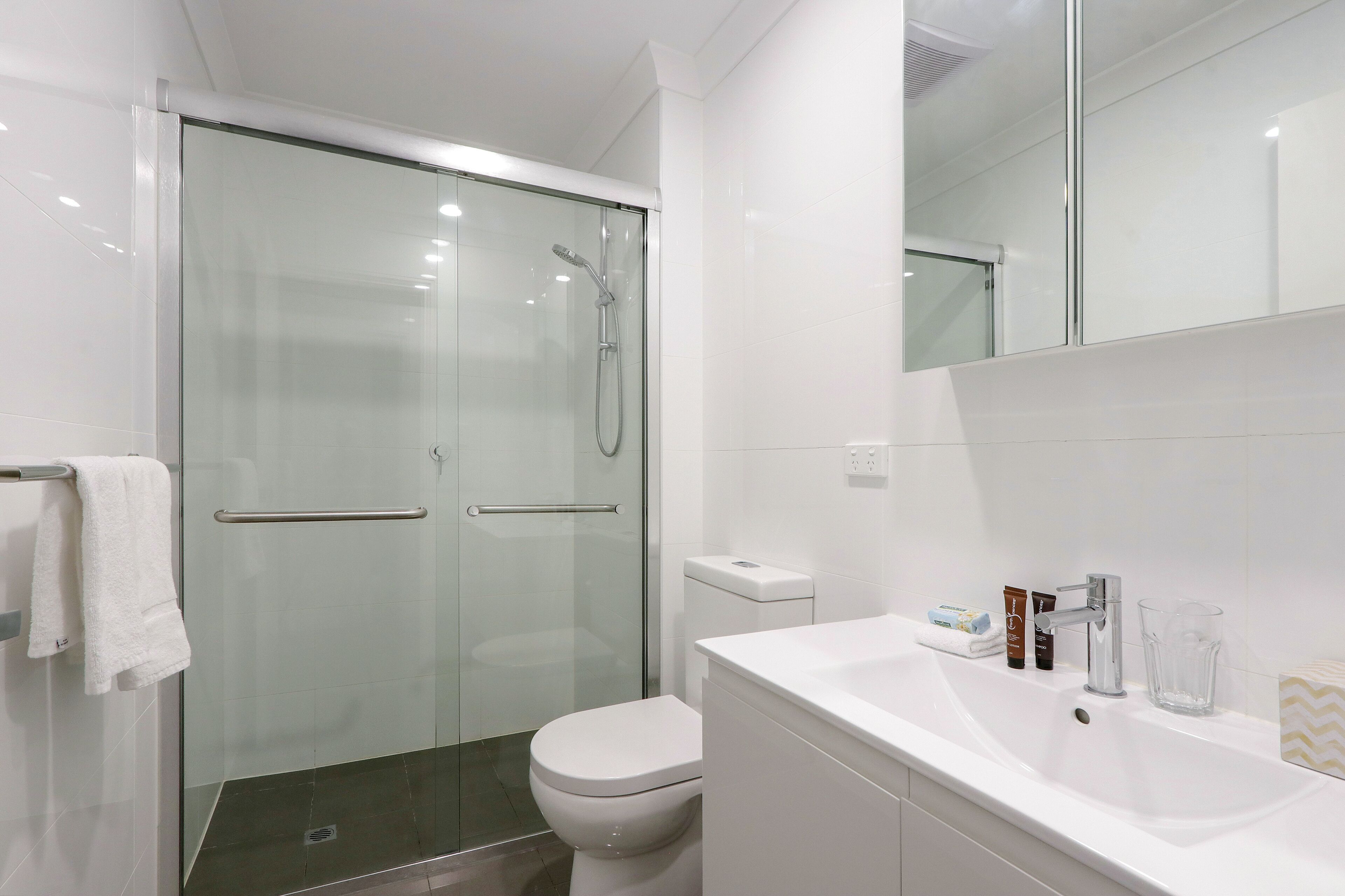 Un bagno moderno con cabina doccia in vetro, un water bianco e un lavandino bianco con articoli da toilette.