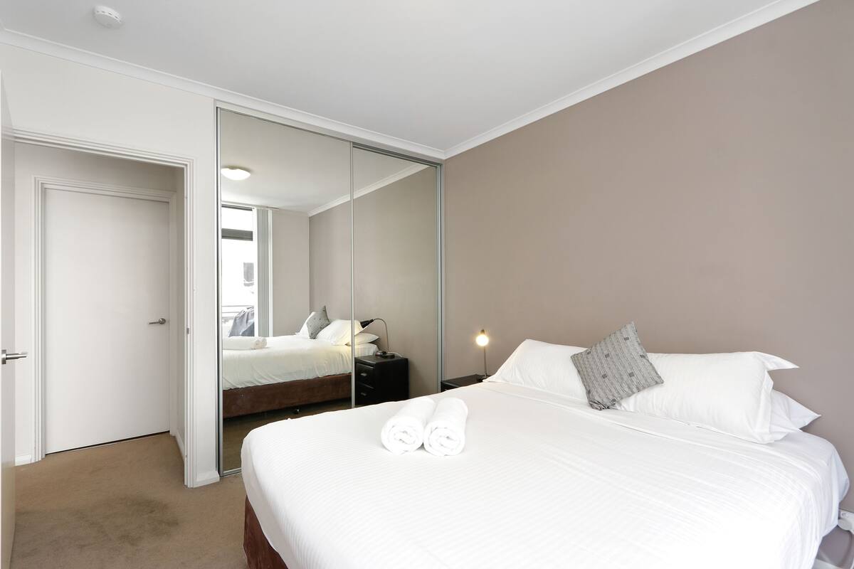 A hotel room with a large bed, a bedside table, a nightstand, a mirror, and a door.