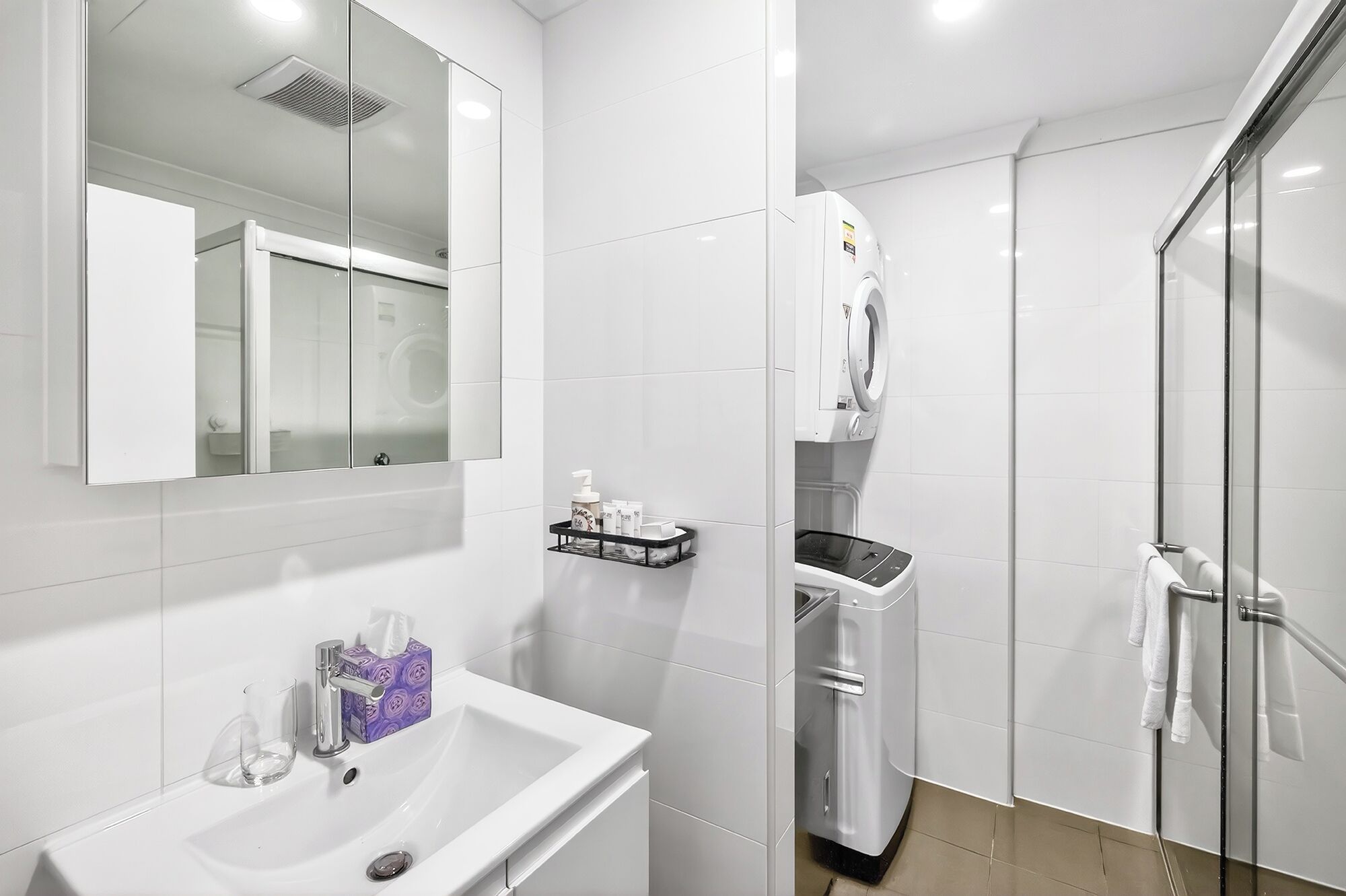 A modern bathroom with a sink, mirror, towel rack, and a glass shower enclosure.