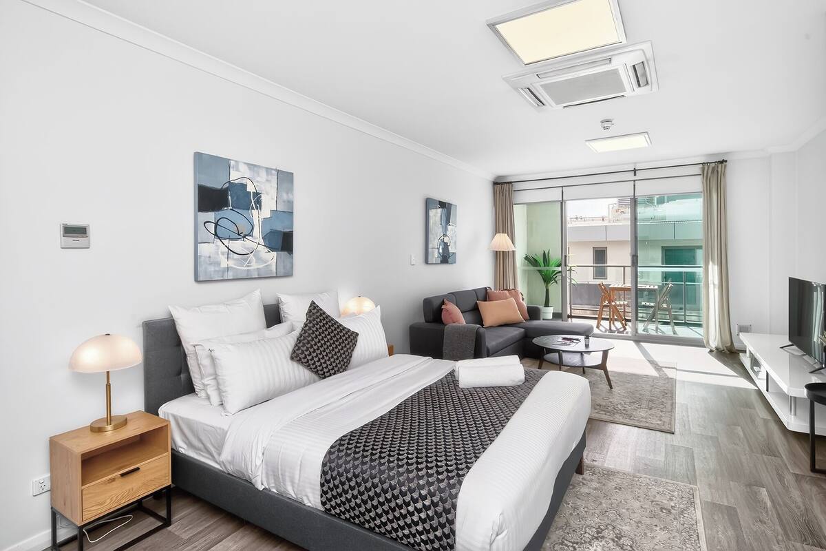 A modern bedroom with a bed, bedside tables, a sofa, a TV, and a balcony with a view.