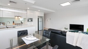 A modern kitchen with white cabinets, a dining table with chairs, a black leather sofa, and a flat-screen TV. - 188 Apartments (Perth)