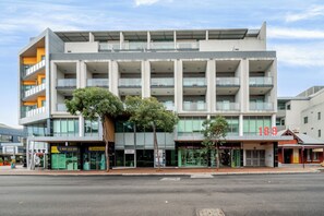 A multi-story building with a modern architectural design, featuring balconies, large windows, and a ground-level commercial space with signage.