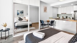 A modern hotel room with a bed, bedside table, and a view through a sliding door to a dining area with a table and chairs. - 188 Apartments (Perth)