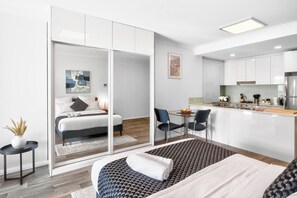 A modern hotel room with a bed, bedside table, and a view through a sliding door to a dining area with a table and chairs. - 188 Apartments (Perth)