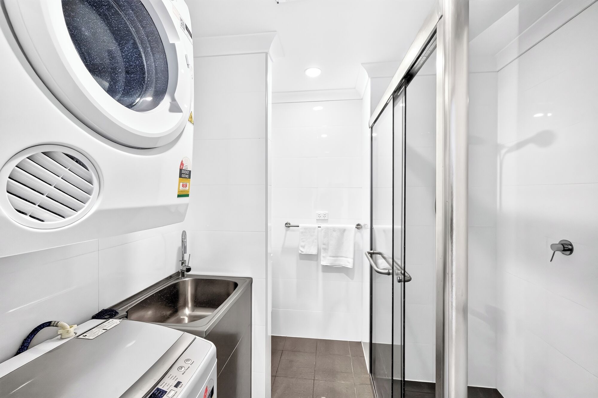 Een moderne badkamer met een ingebouwde wasmachine, een glazen douchecabine en een wastafel.