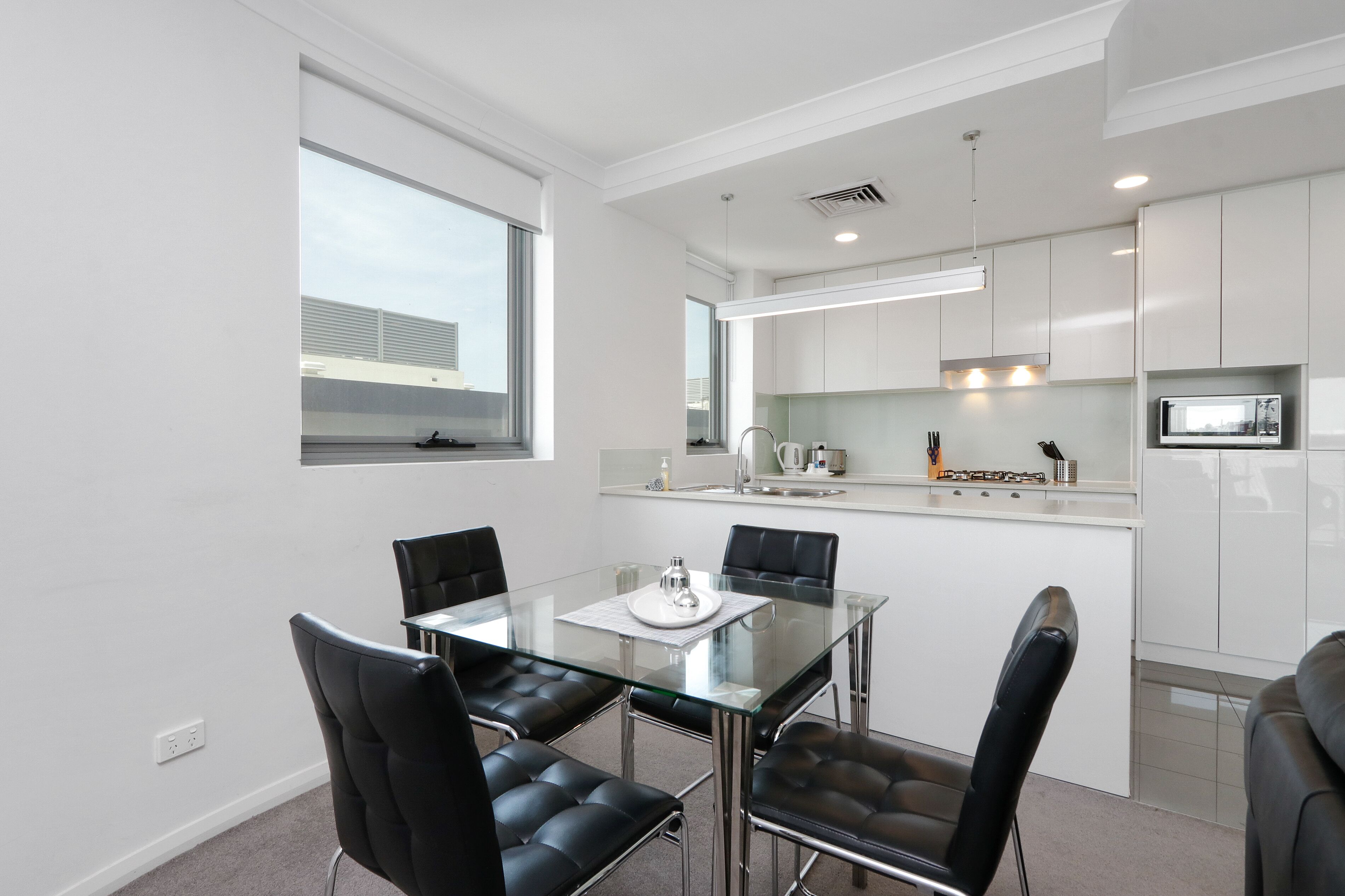 A modern kitchen with white cabinets, a glass dining table, and black chairs.
