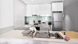 A modern kitchen with white cabinets, stainless steel appliances, and a central island with a sink and a vase of flowers. - 188 Apartments (Perth)