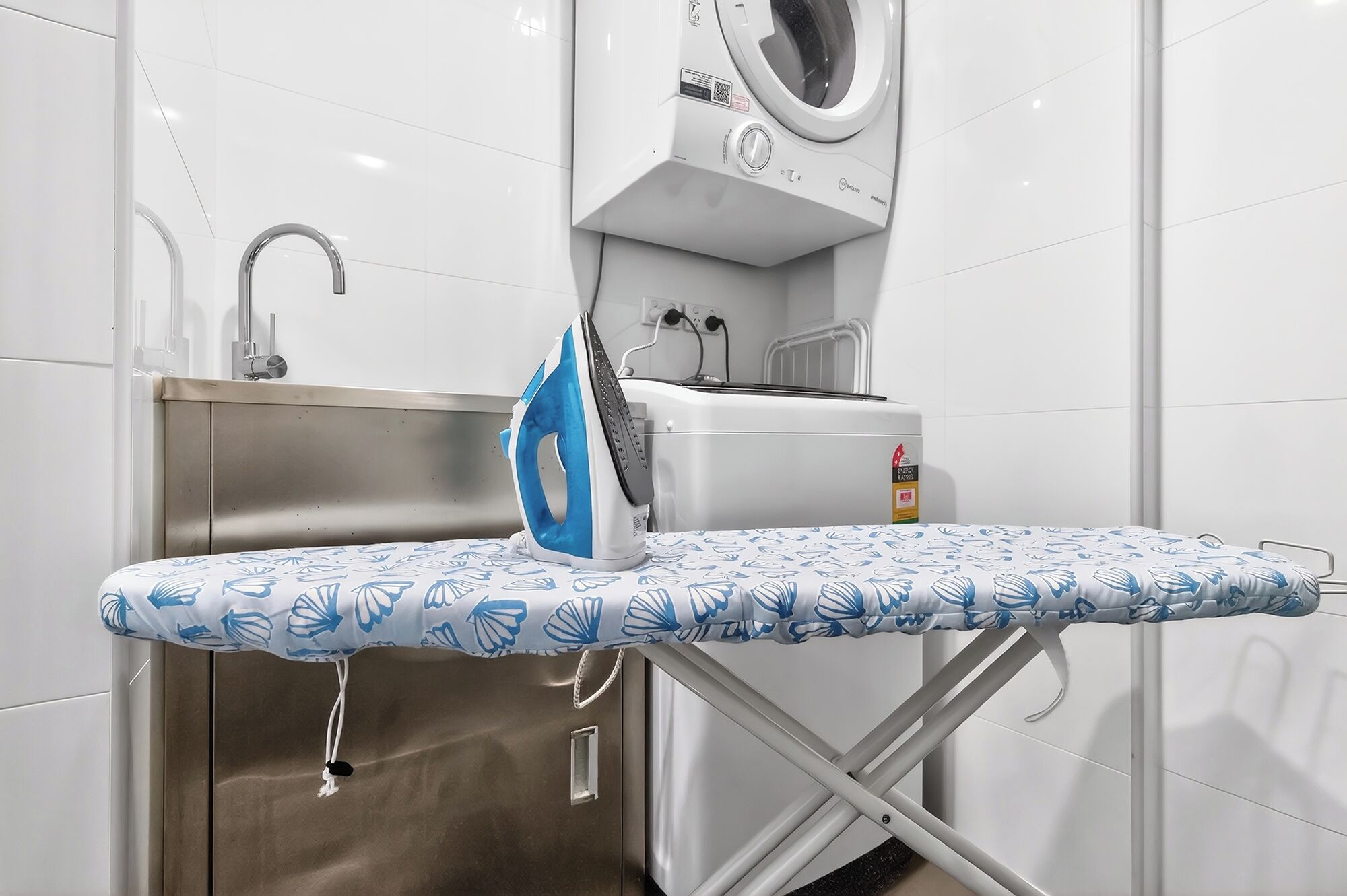 Ein kompaktes Hotelzimmer mit Waschmaschine, Spüle und Bügelbrett.