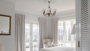 A bedroom with a large bed, a chair, a chandelier, and a view through the window. - Goodin Country Garden (Warea)