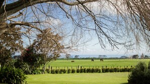 A grassy field with a fence, trees, and a distant view of the sea. - Goodin Country Garden (Warea)