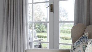 A room with a white door, a white chair, and a view of a garden. - Goodin Country Garden (Warea)