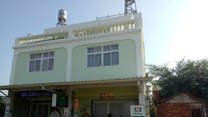 A two-story building with a green facade, a water tank on the roof, and a small outdoor seating area with tables and chairs.