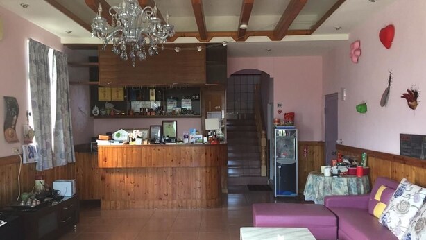 A hotel lobby with a wooden reception desk, a staircase, a purple sofa, and a chandelier.