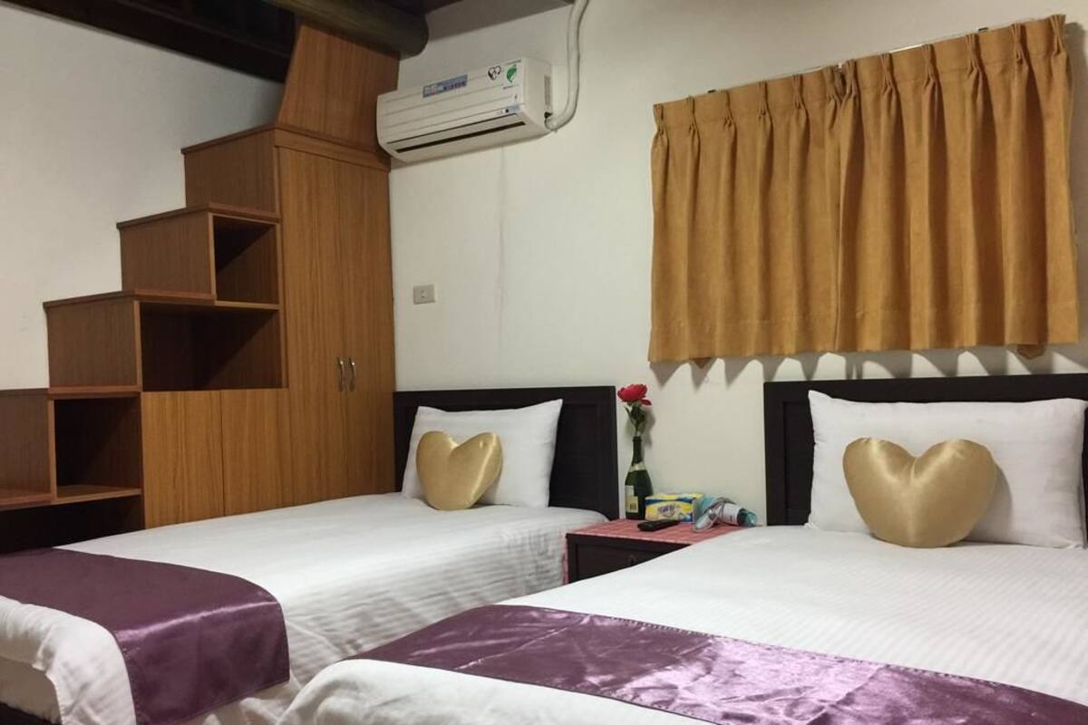 A hotel room with two beds, a wardrobe, a nightstand, and a window with curtains.