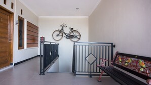 A hallway with a wooden door, a bench with colorful metalwork, and a bicycle mounted on the wall. - Hotel O Al Abror Homestay (Yogyakarta)