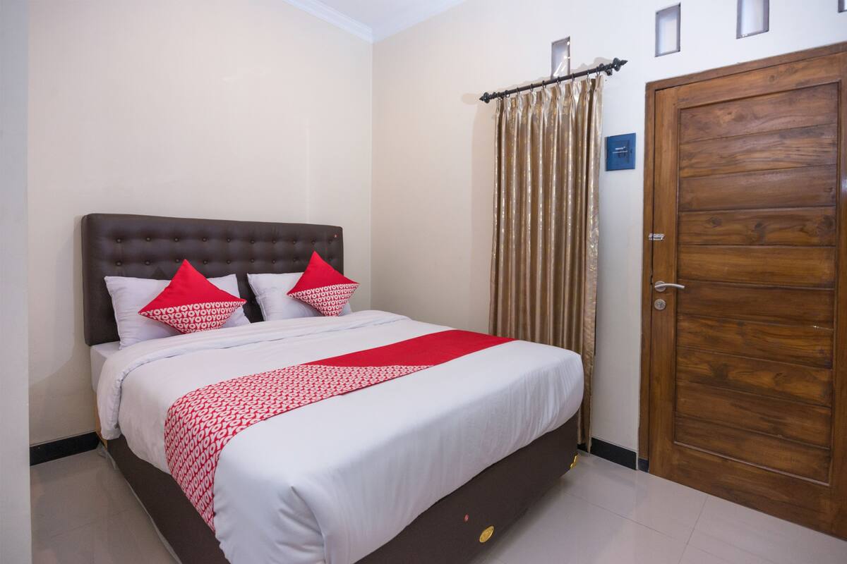 A neatly made bed with a red and white patterned bedspread, two pillows, and a wooden headboard.