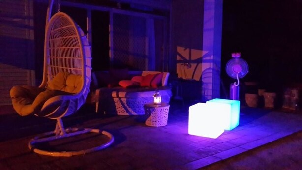 A porch with a hanging chair, a cushioned bench, a small table with a candle, and a glowing cube. - Rong Shu Xia B&B (Jinning)