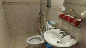 A bathroom with a toilet, bidet, and sink. There are orange cups on a shelf and a tissue box on the toilet. - Rong Shu Xia B&B (Jinning)