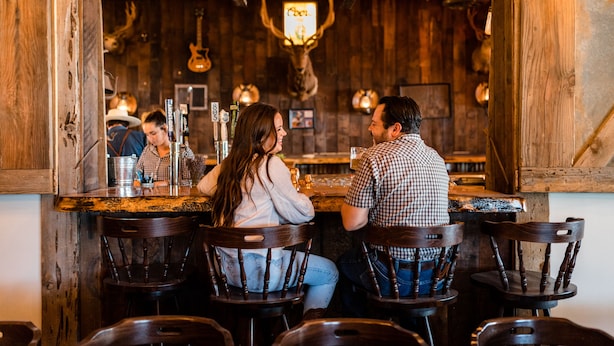 A rustic bar with wooden walls, a mounted deer head, and a counter with bottles and glasses. - Cuyama Buckhorn (New Cuyama)