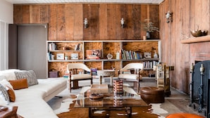 A cozy living room with a white sofa, leather ottoman, and a glass coffee table. There are two white armchairs, a wooden bookshelf filled with books, and a fireplace. - Cuyama Buckhorn (New Cuyama)