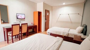 Una habitación de hotel con dos camas, un escritorio con sillas, un televisor y un armario.