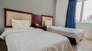 Habitación de hotel con dos camas individuales, cabecera de madera, mesita de noche y ventana con cortinas azules.