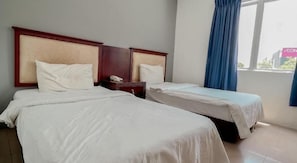 Ein Hotelzimmer mit zwei Einzelbetten, einem hölzernen Kopfteil, einem Nachttisch und einem Fenster mit blauen Vorhängen.