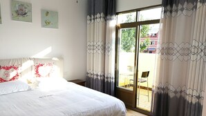 A bedroom with a large bed, a sliding glass door to an outdoor area, and a view of a building outside. - 37 Garden Guesthouse Shilin Family (Kunming)