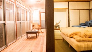 A traditional Japanese-style room with tatami flooring, a low wooden bed with a yellow blanket, a wooden table, and a chair. - Engawa (Tonosho)