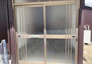 A metal gate with a frosted glass panel and a sign. - Engawa (Tonosho)