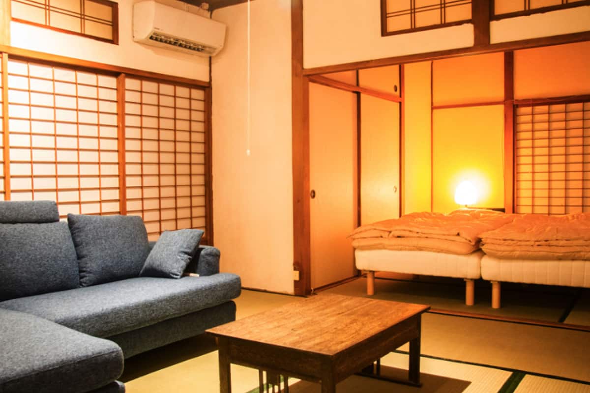 A traditional Japanese room with tatami flooring, a low wooden table, a sofa, and sliding doors leading to a bed area.
