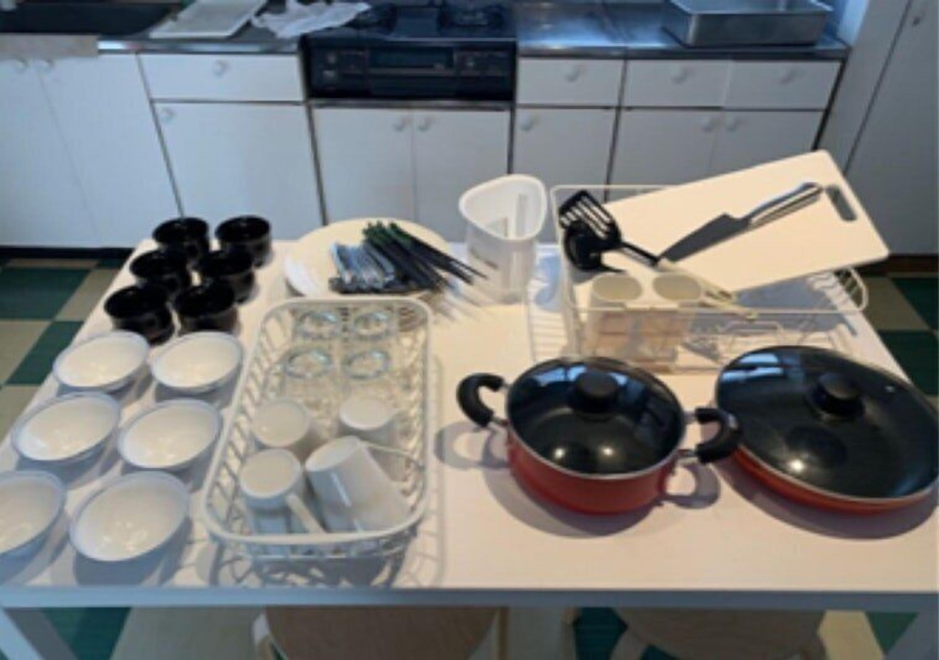 A kitchen with white cabinets, a countertop with various kitchen utensils, a kettle, and a pot.