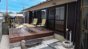 A wooden deck with two chairs and a table, a stone bench, and a stone planter. - Engawa (Tonosho)