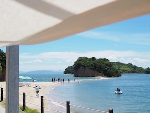 A beach with people walking, a jet ski, and a cliff with greenery. - Engawa (Tonosho)