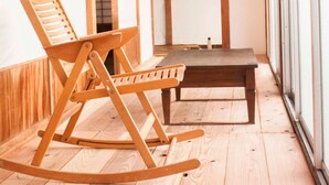 A room with wooden flooring, a rocking chair, a small table, and large windows. - Engawa (Tonosho)