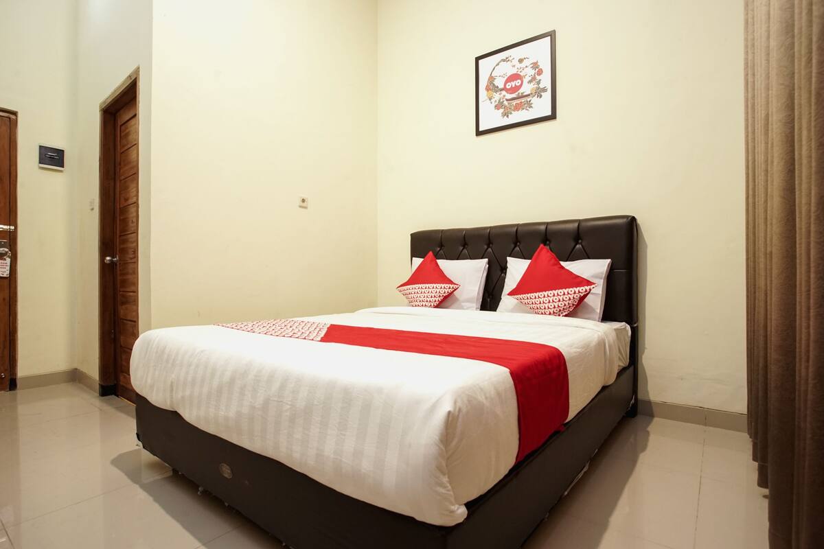 A neatly made bed with a red and white bedspread, a black headboard, and two red pillows.