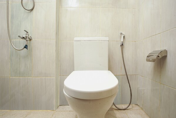 A bathroom with a toilet, a shower, and a toilet paper holder. - OYO 1241 Eirini Family Homestay (Depok)