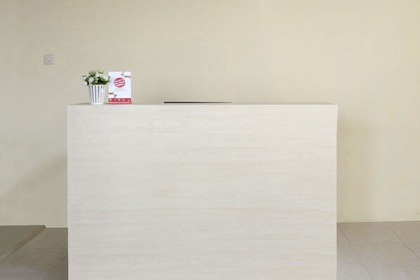 En receptionsdisk med lyse trædetaljer, en hvid vase med blomster og et rødt og hvidt informationskort.
