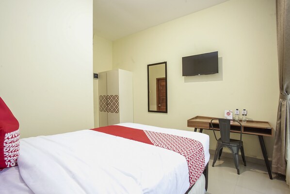 A hotel room with a bed, a desk, a chair, a television, and a mirror. - OYO 1241 Eirini Family Homestay (Depok)