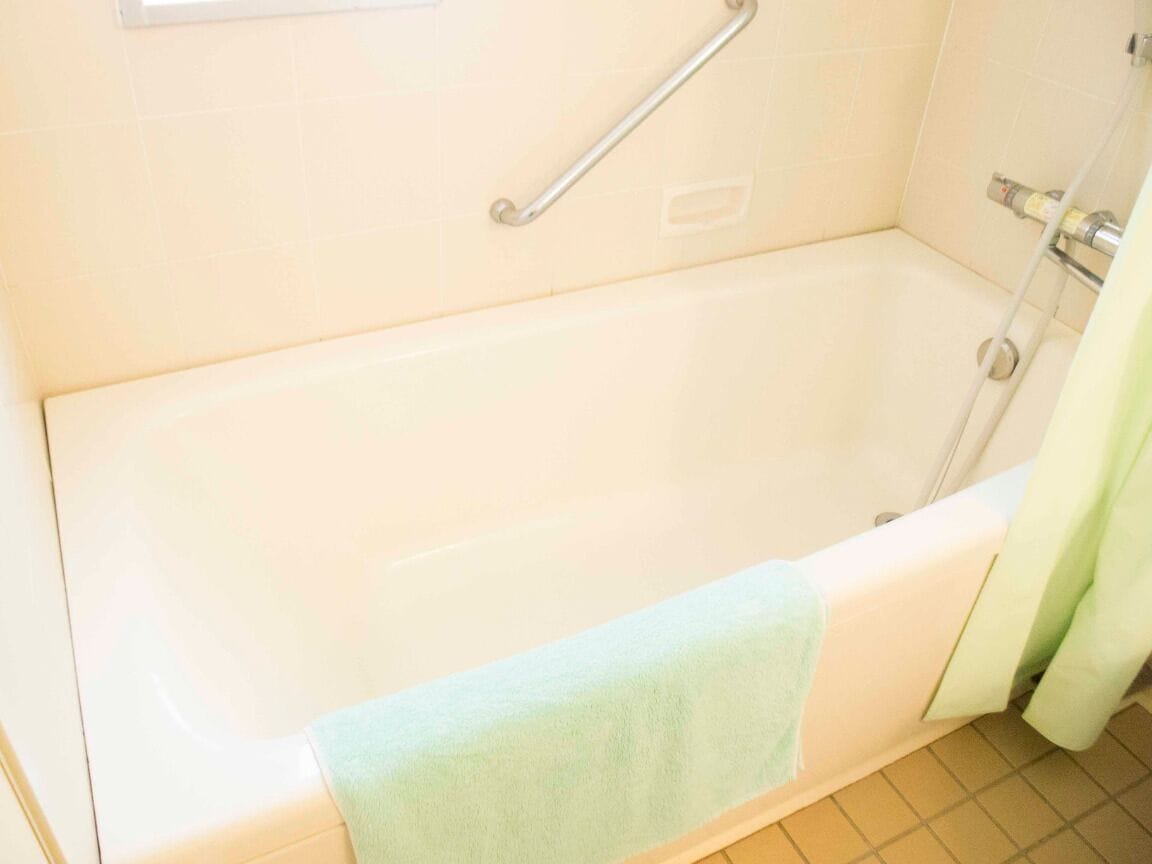 Una bañera con una barra de apoyo, una toalla y una cortina de ducha.