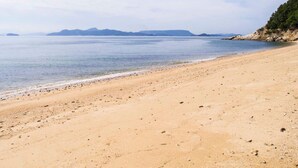 A wide sandy beach with calm water and distant mountains. - Irou (Tonosho)