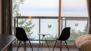 A room with a balcony overlooking a body of water, featuring two chairs and a small table. - Irou (Tonosho)
